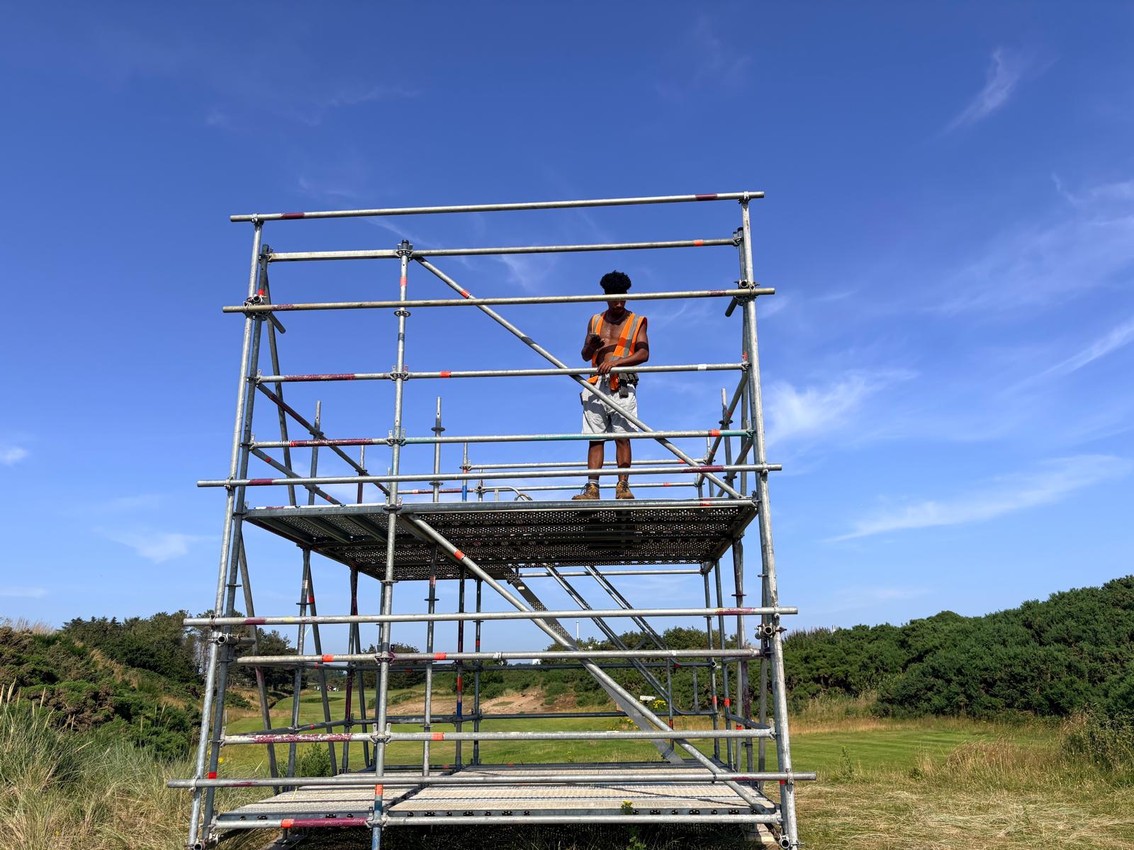 Scaffolder in high-vis standing on a galvanised scaffold tower on a UK golf course