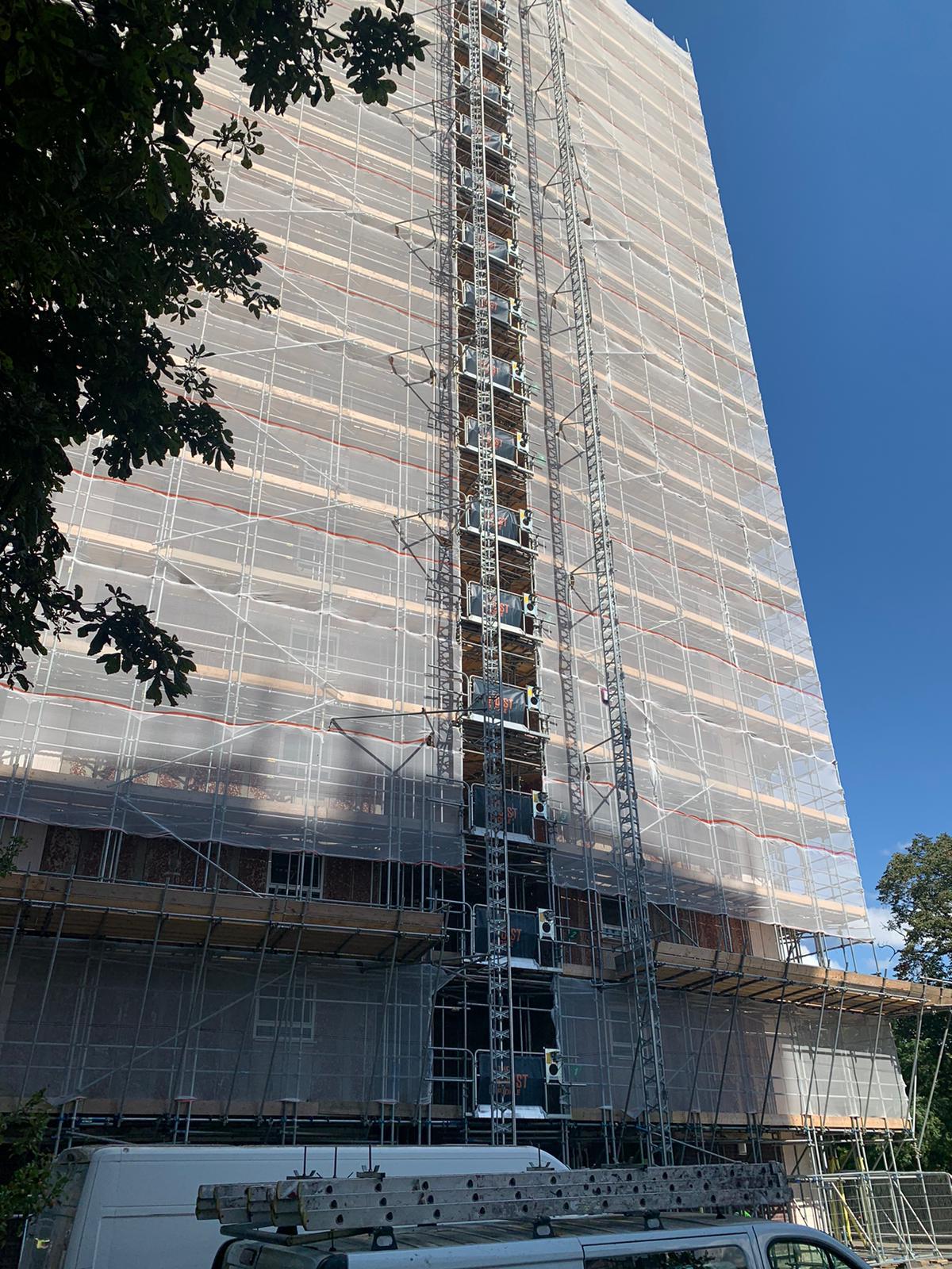 Clear debris netting wrapping a high-rise scaffold with a materials hoist