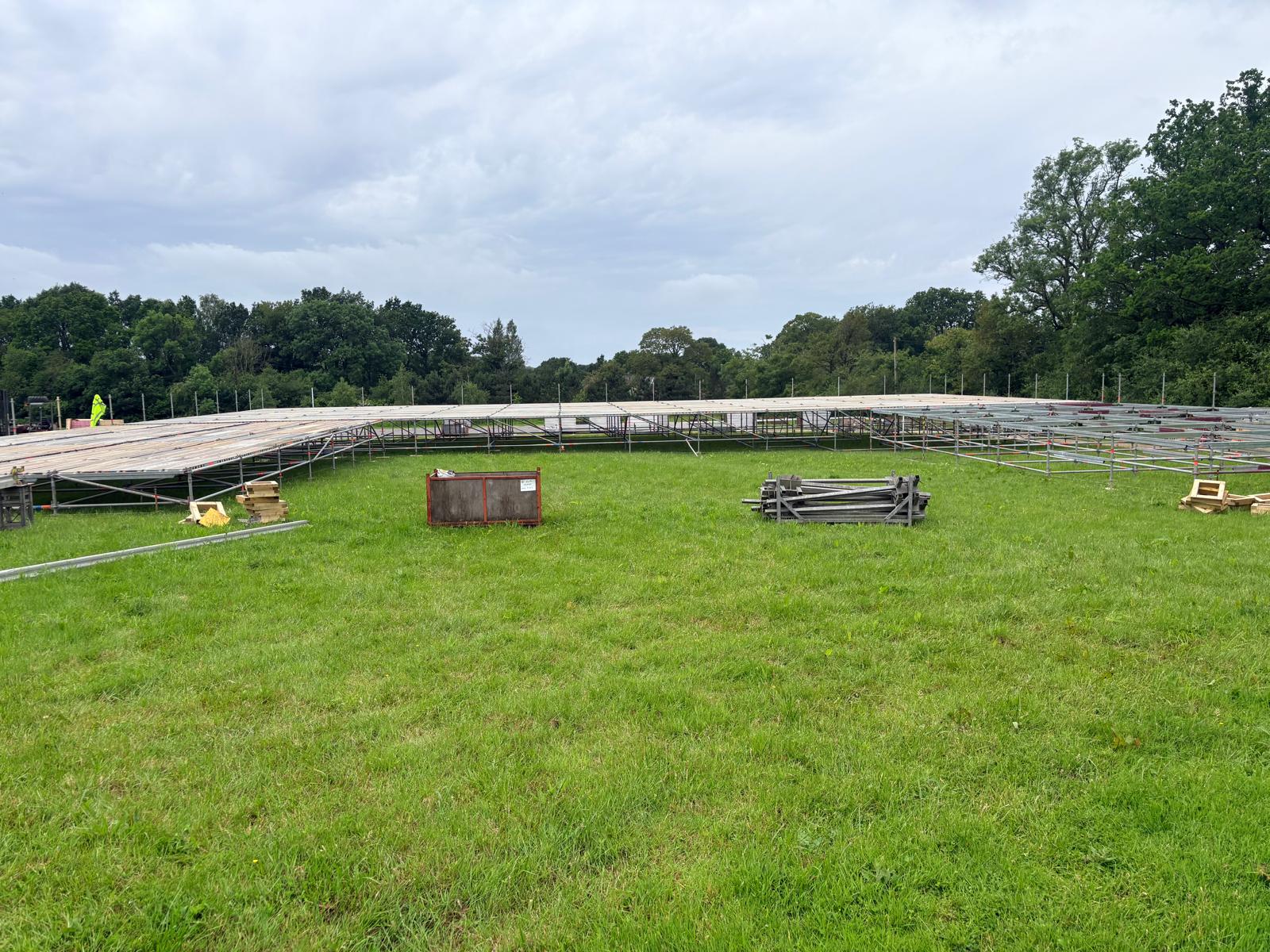 Timber-decked scaffold event platform being assembled across a grass field