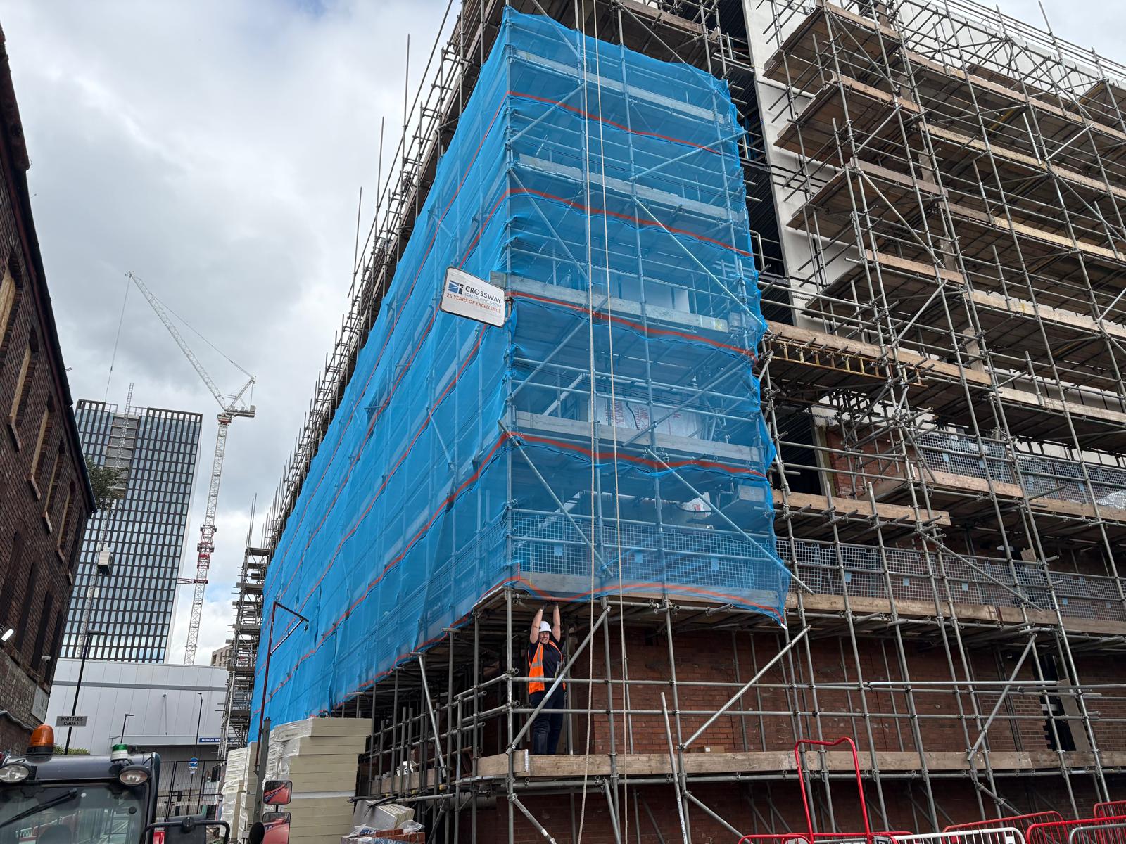 Blue debris netting wrapping a multi-storey scaffold on a UK building site