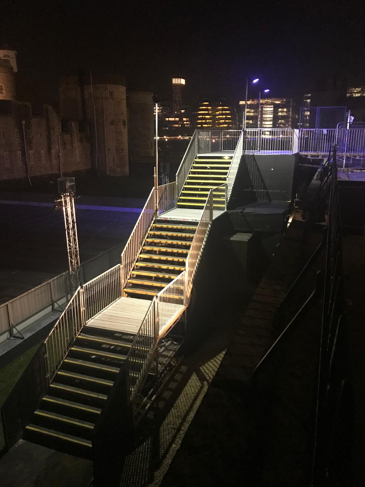 Lit metal event staircase with yellow-nosed treads at night