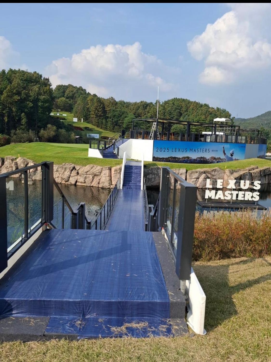 Pedestrian bridge with a blue deck spanning water at a golf event